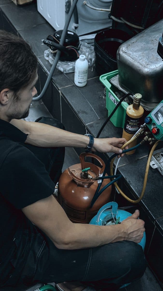 A refrigeration technician connecting gauges and refrigerant cylinders at a workbench