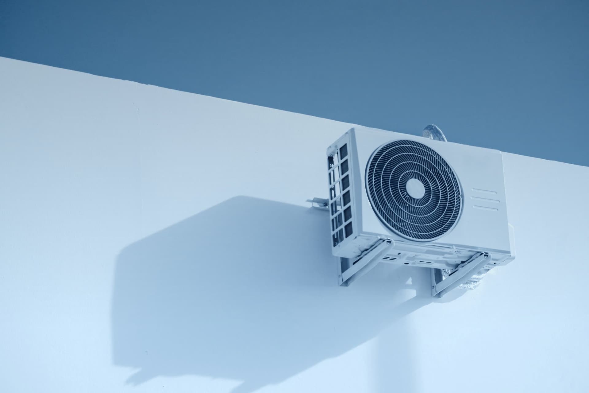 An outdoor air conditioning unit mounted on a white wall under a blue sky