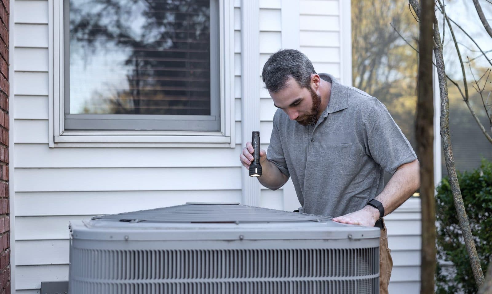 A technician inspecting an outdoor air conditioning unit with a torch